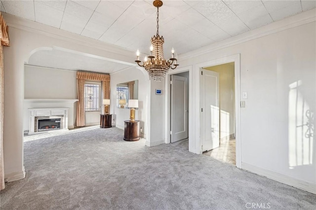 unfurnished living room with crown molding, an inviting chandelier, carpet floors, a high end fireplace, and baseboards
