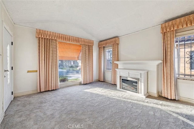 unfurnished living room featuring baseboards, carpet, a textured ceiling, vaulted ceiling, and a glass covered fireplace