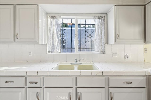 kitchen with a sink, backsplash, light countertops, and white cabinetry