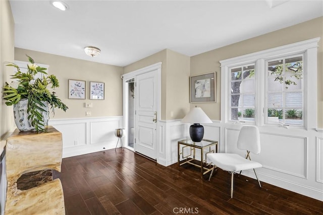living area featuring a wainscoted wall, a decorative wall, and dark wood finished floors