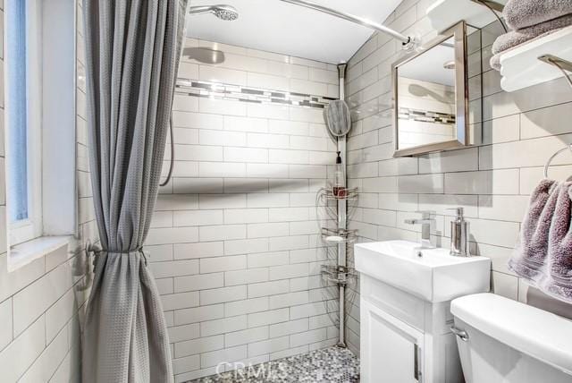 full bathroom with toilet, tiled shower, vanity, and tile walls