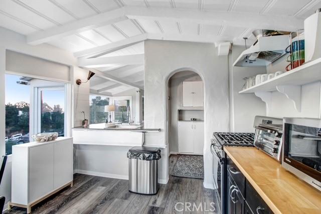 kitchen with arched walkways, appliances with stainless steel finishes, wood finished floors, vaulted ceiling with beams, and wood counters