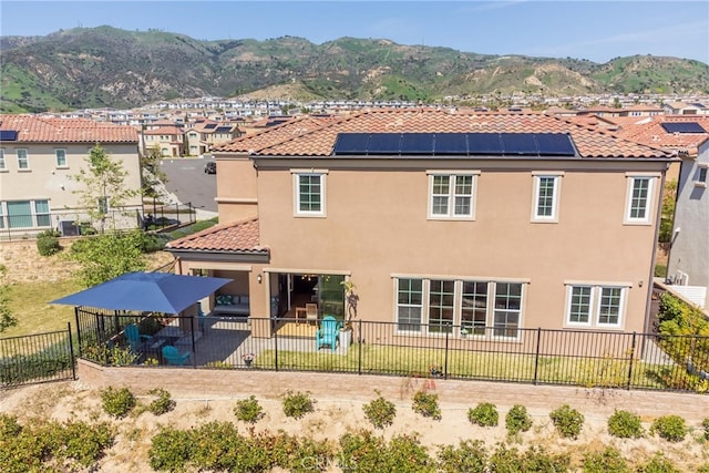 back of house featuring a tiled roof, a fenced backyard, a mountain view, stucco siding, and solar panels