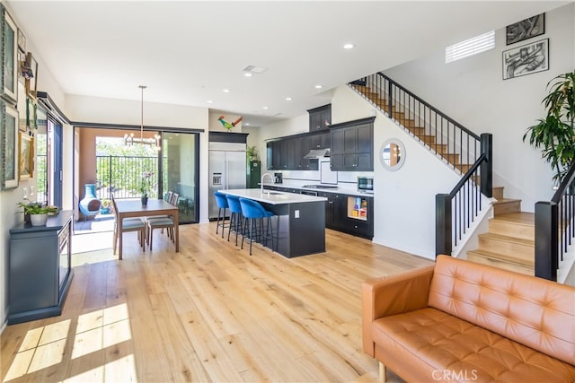 kitchen featuring light wood-type flooring, a kitchen bar, built in appliances, light countertops, and an island with sink