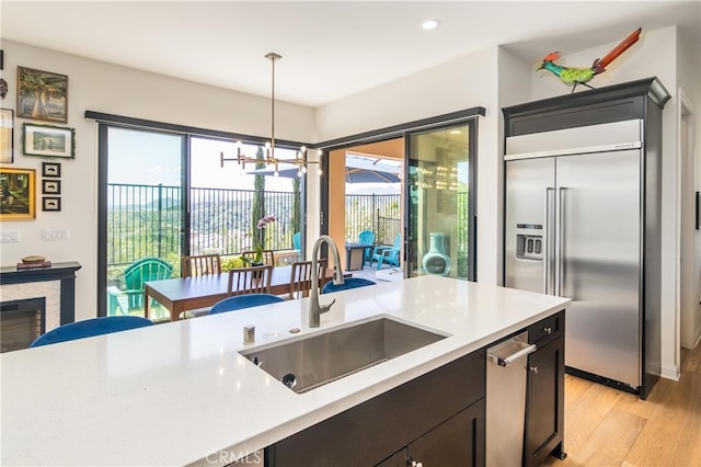 kitchen with stainless steel built in refrigerator, light wood-style floors, a sink, and light countertops