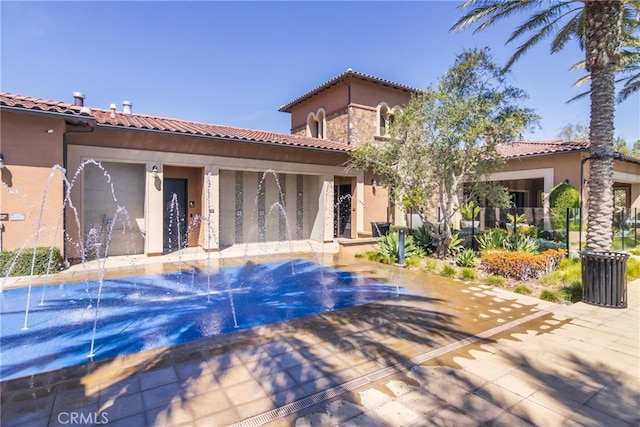 rear view of house with a pool, a tile roof, and stucco siding