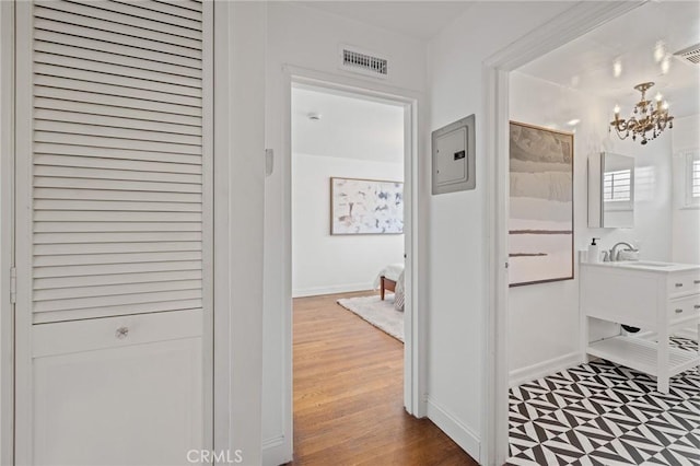 hall with electric panel, visible vents, a chandelier, wood finished floors, and a sink