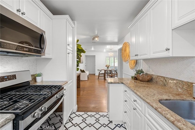 kitchen featuring tasteful backsplash, a sink, white cabinetry, light stone countertops, and stainless steel appliances