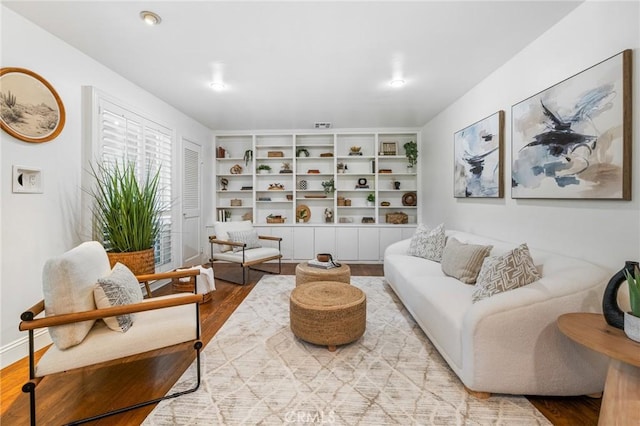 living room with built in shelves, baseboards, and wood finished floors