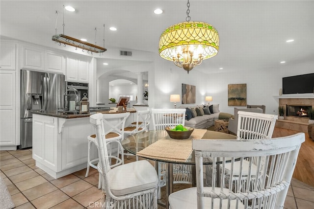 dining room featuring visible vents, light tile patterned floors, arched walkways, a fireplace, and recessed lighting