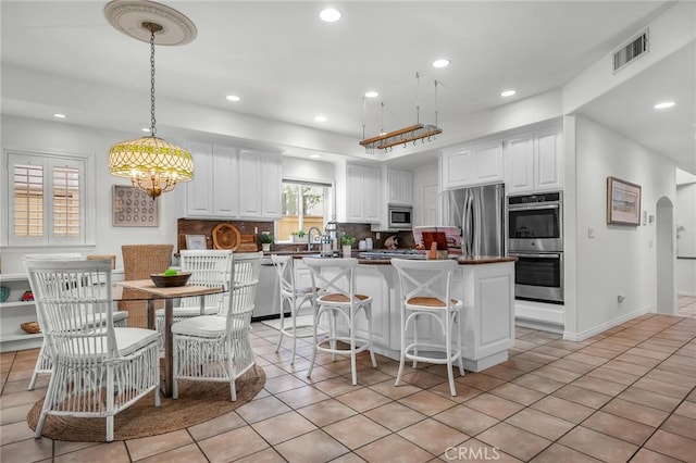 kitchen with tasteful backsplash, visible vents, white cabinetry, stainless steel appliances, and light tile patterned flooring