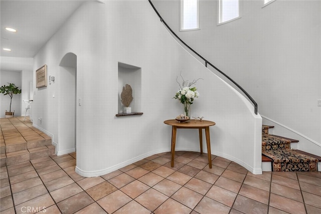 entryway with light tile patterned floors, arched walkways, recessed lighting, a towering ceiling, and stairs