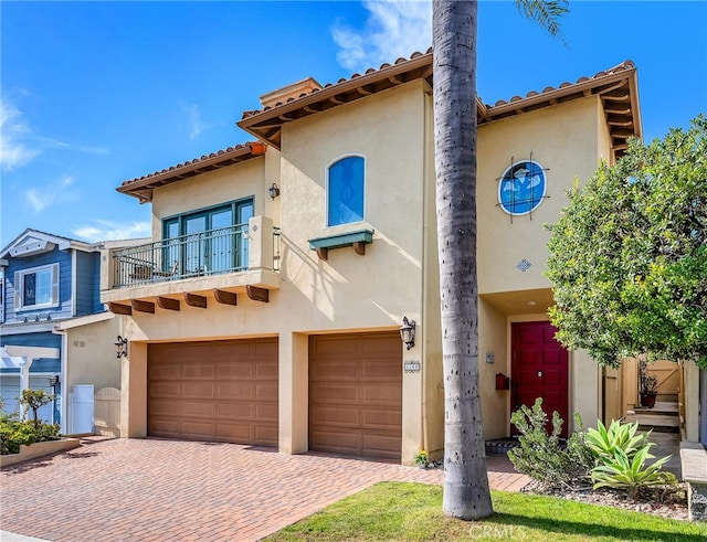 mediterranean / spanish house with stucco siding, decorative driveway, a garage, and a balcony