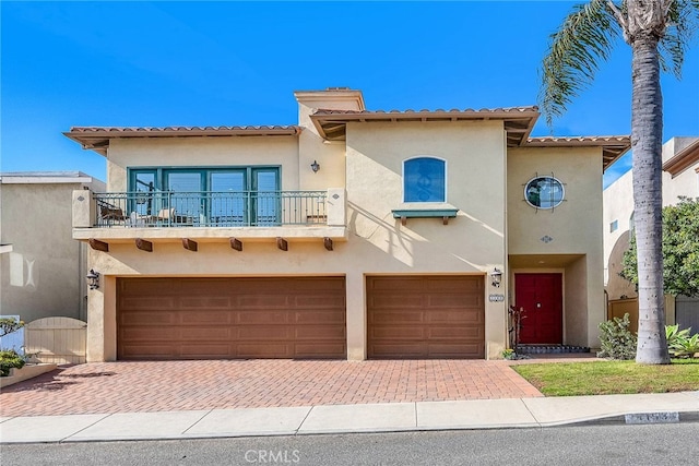 mediterranean / spanish house with a balcony, stucco siding, decorative driveway, and an attached garage