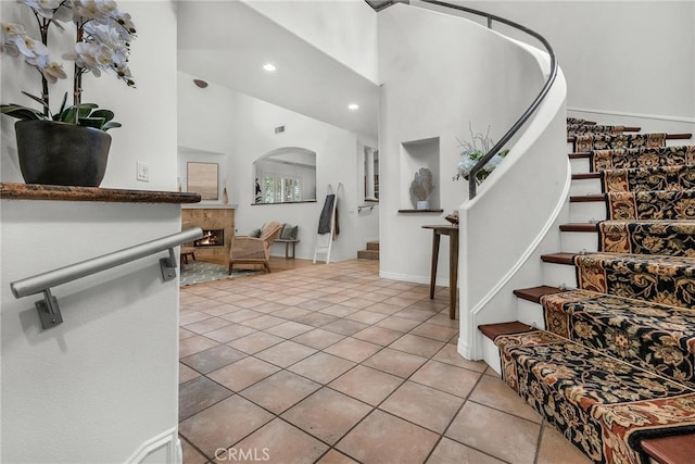 entrance foyer featuring recessed lighting, a high ceiling, light tile patterned flooring, stairs, and arched walkways