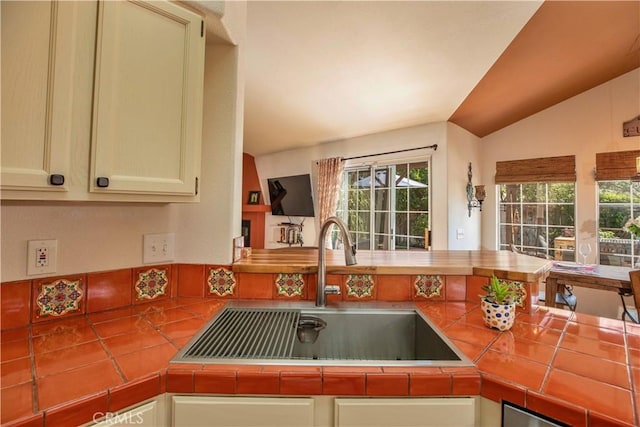 kitchen with a sink, vaulted ceiling, and tile counters