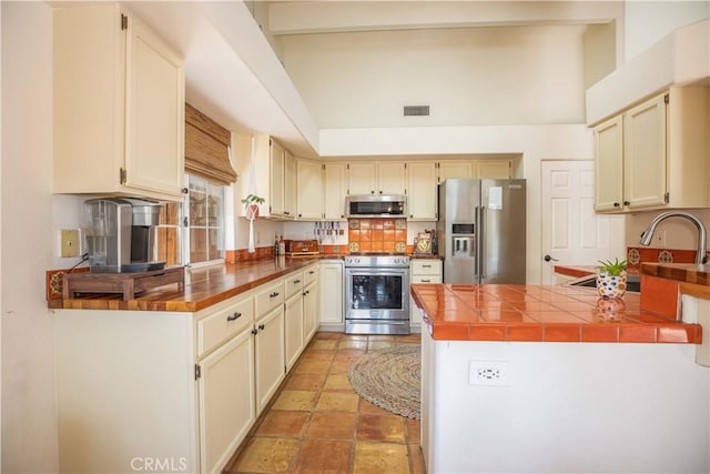 kitchen featuring a peninsula, high vaulted ceiling, visible vents, beamed ceiling, and appliances with stainless steel finishes