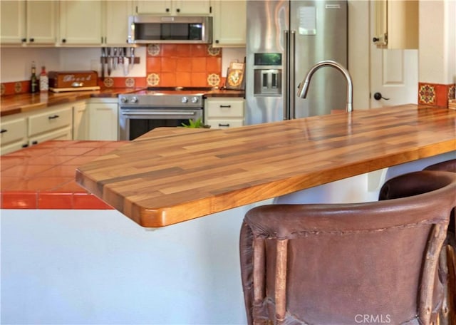 kitchen featuring butcher block countertops, a peninsula, a kitchen breakfast bar, and appliances with stainless steel finishes