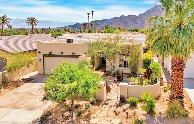 pueblo revival-style home featuring a mountain view, an attached garage, stucco siding, concrete driveway, and a gate