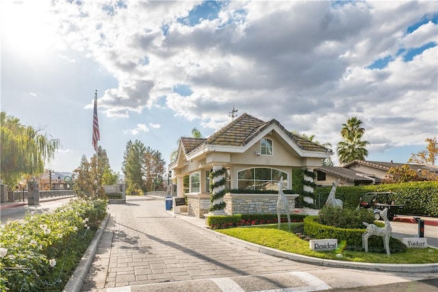 exterior space featuring a tile roof, stone siding, stucco siding, and fence