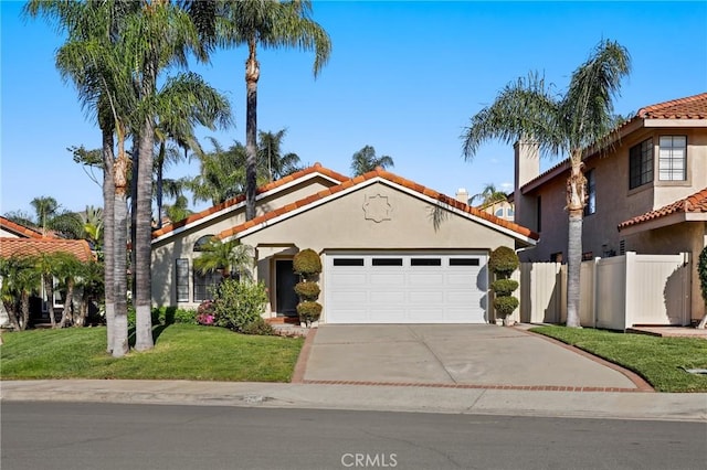 mediterranean / spanish-style house with stucco siding, driveway, an attached garage, a tiled roof, and fence