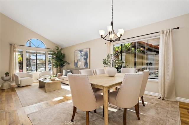 dining area featuring a chandelier, high vaulted ceiling, light wood finished floors, and baseboards