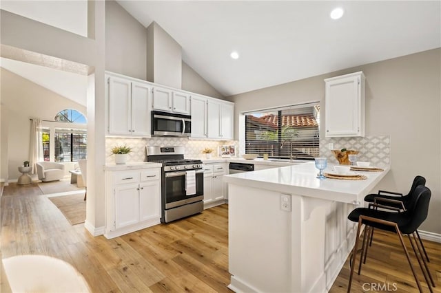 kitchen featuring a peninsula, light countertops, white cabinets, appliances with stainless steel finishes, and light wood finished floors