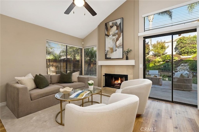 living room with a tiled fireplace, ceiling fan, high vaulted ceiling, and light wood-style flooring