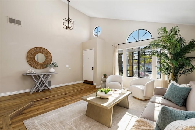 living area with high vaulted ceiling, visible vents, light wood-type flooring, and baseboards