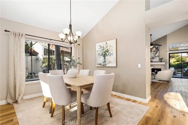 dining space featuring light wood-style floors, high vaulted ceiling, an inviting chandelier, and baseboards