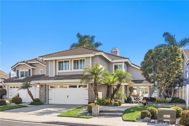 traditional-style home featuring a chimney, fence, a tiled roof, concrete driveway, and an attached garage