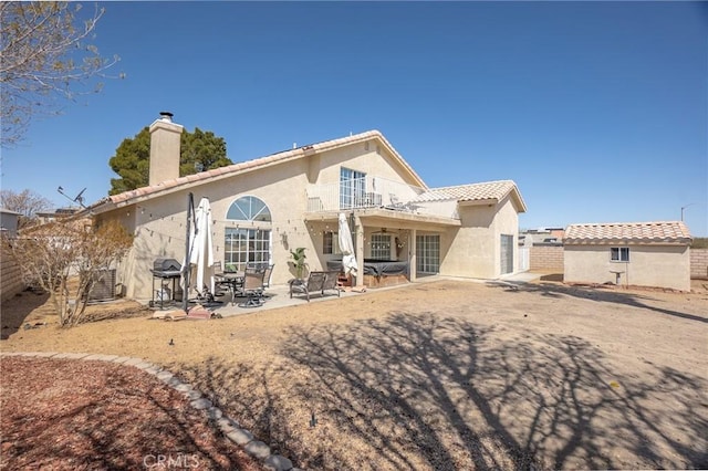 rear view of property featuring fence, a balcony, a chimney, and stucco siding