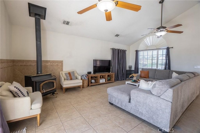 living area with a wood stove, visible vents, a ceiling fan, and light tile patterned flooring