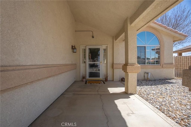 property entrance with a patio, stucco siding, and fence