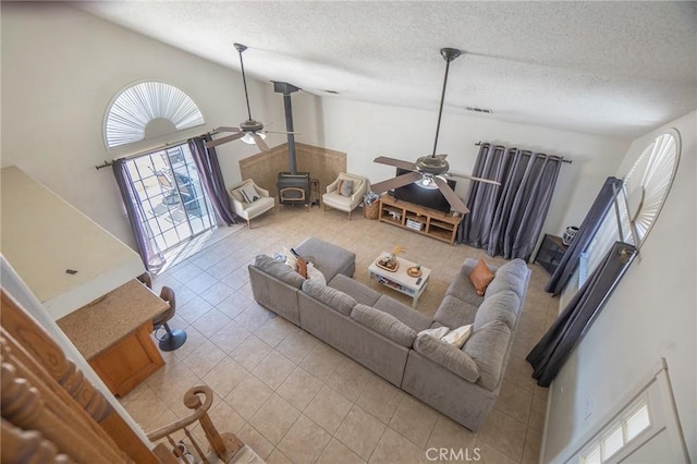 living room with a textured ceiling, a wood stove, a ceiling fan, and tile patterned floors