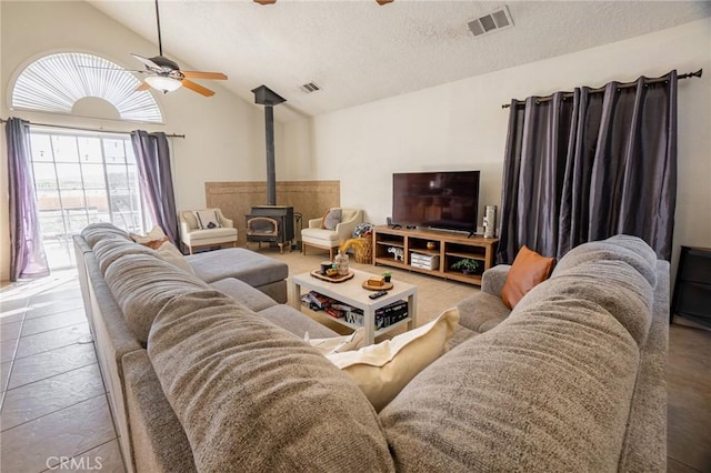 living room featuring vaulted ceiling, a textured ceiling, a wood stove, visible vents, and ceiling fan