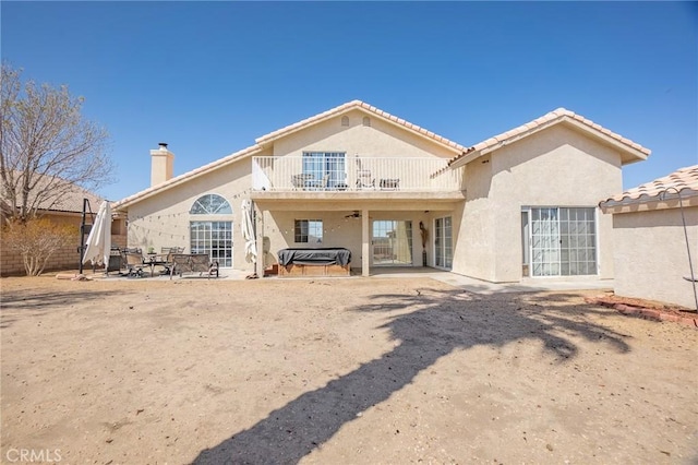 back of house featuring a chimney, a tile roof, a patio, stucco siding, and a balcony