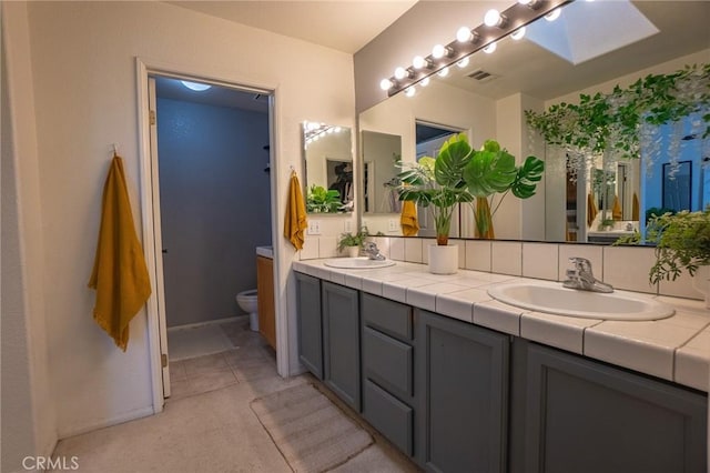 bathroom featuring double vanity, a sink, toilet, and a skylight