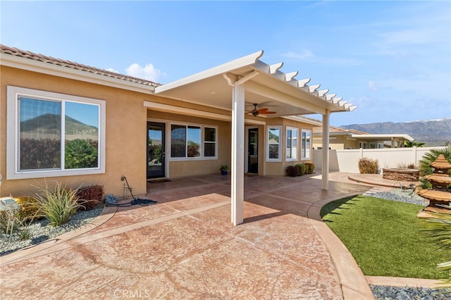 rear view of property featuring stucco siding, a mountain view, a patio area, ceiling fan, and fence
