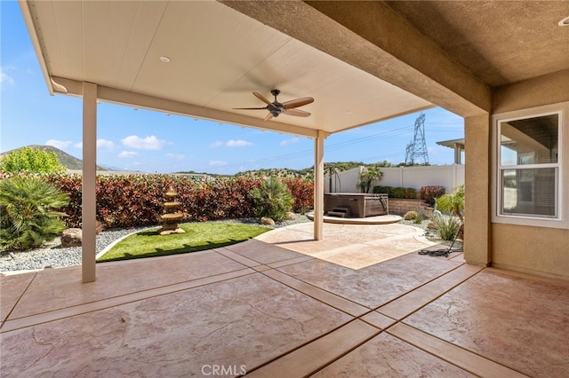 view of patio featuring a hot tub, fence, and a ceiling fan