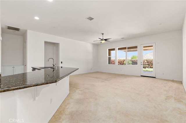 unfurnished living room featuring a sink, visible vents, a ceiling fan, and light carpet
