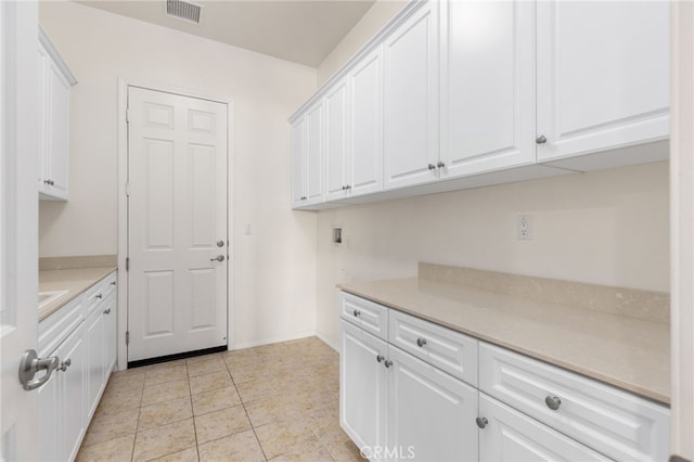laundry area with visible vents, baseboards, cabinet space, and light tile patterned floors