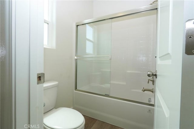 bathroom with wood finished floors, bath / shower combo with glass door, and toilet