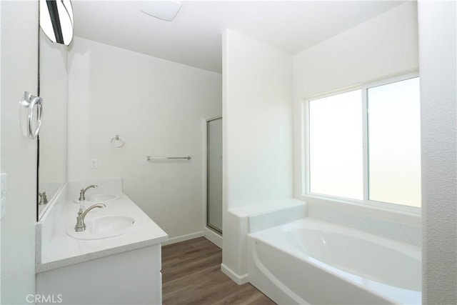 full bathroom with a garden tub, wood finished floors, a sink, a stall shower, and double vanity