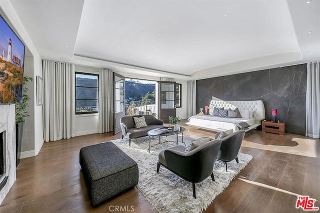 bedroom featuring a fireplace, a tray ceiling, an accent wall, wood finished floors, and baseboards