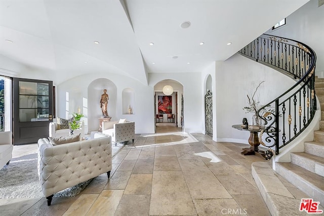 entrance foyer featuring a towering ceiling, recessed lighting, stone tile flooring, stairs, and arched walkways
