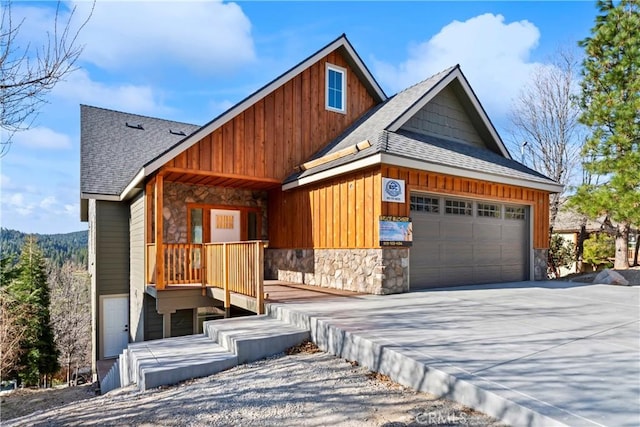 view of front facade with board and batten siding, roof with shingles, stone siding, an attached garage, and concrete driveway