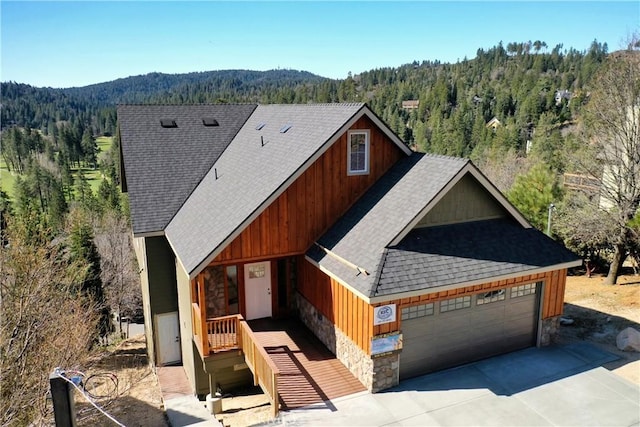 view of front of home featuring a forest view, a shingled roof, and stone siding