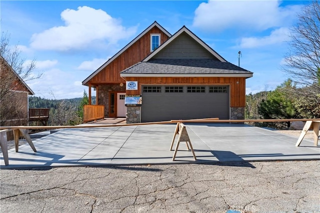 view of front of property featuring a garage, an outdoor structure, a shingled roof, stone siding, and driveway