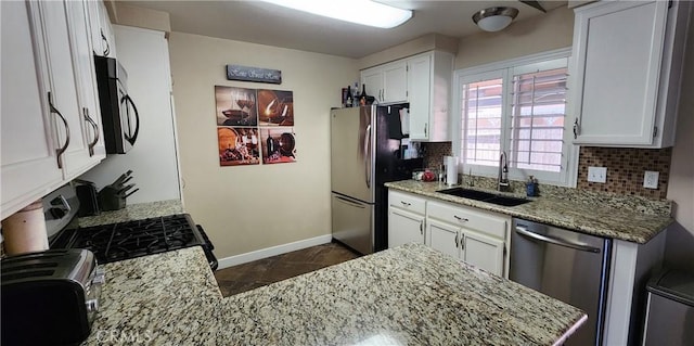 kitchen featuring light stone countertops, tasteful backsplash, a sink, stainless steel appliances, and baseboards